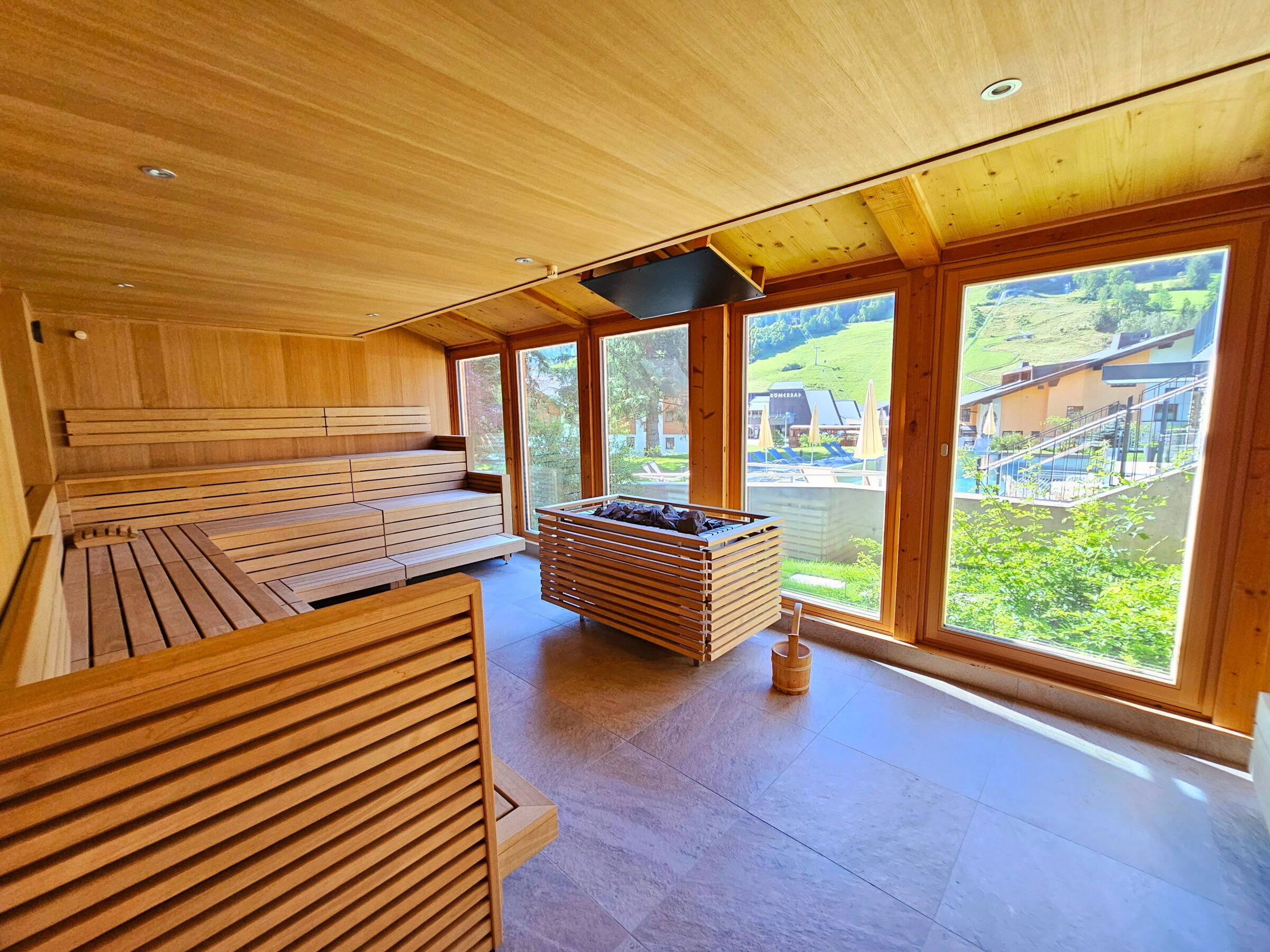 Innenansicht einer Holzsauna mit großen Fenstern zum Gartenbereich für entspannende Erholung.