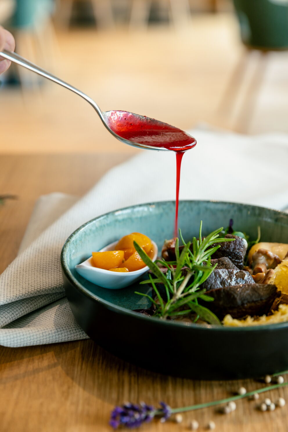 Eine Hand träufelt eine rote Sauce über ein kulinarisches Gericht in einer Schüssel.