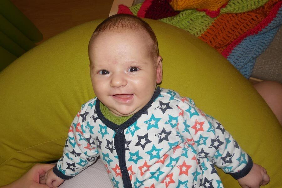 Il bambino Sebastian è sdraiato su un cuscino e sorride.