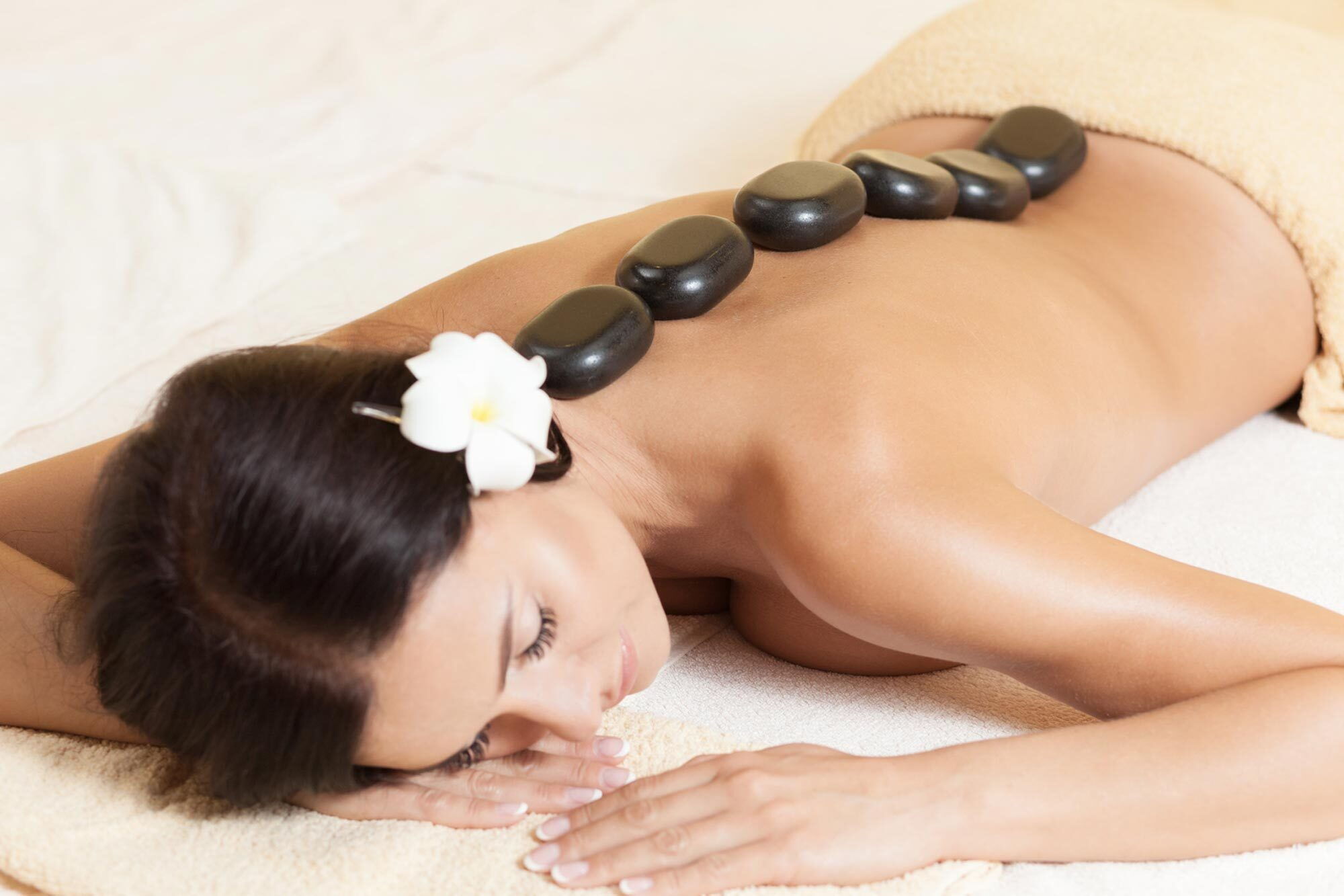 Eine Frau erhält eine Hot Stone Massage mit glatten Steinen auf ihrem Rücken und einer Blume im Haar