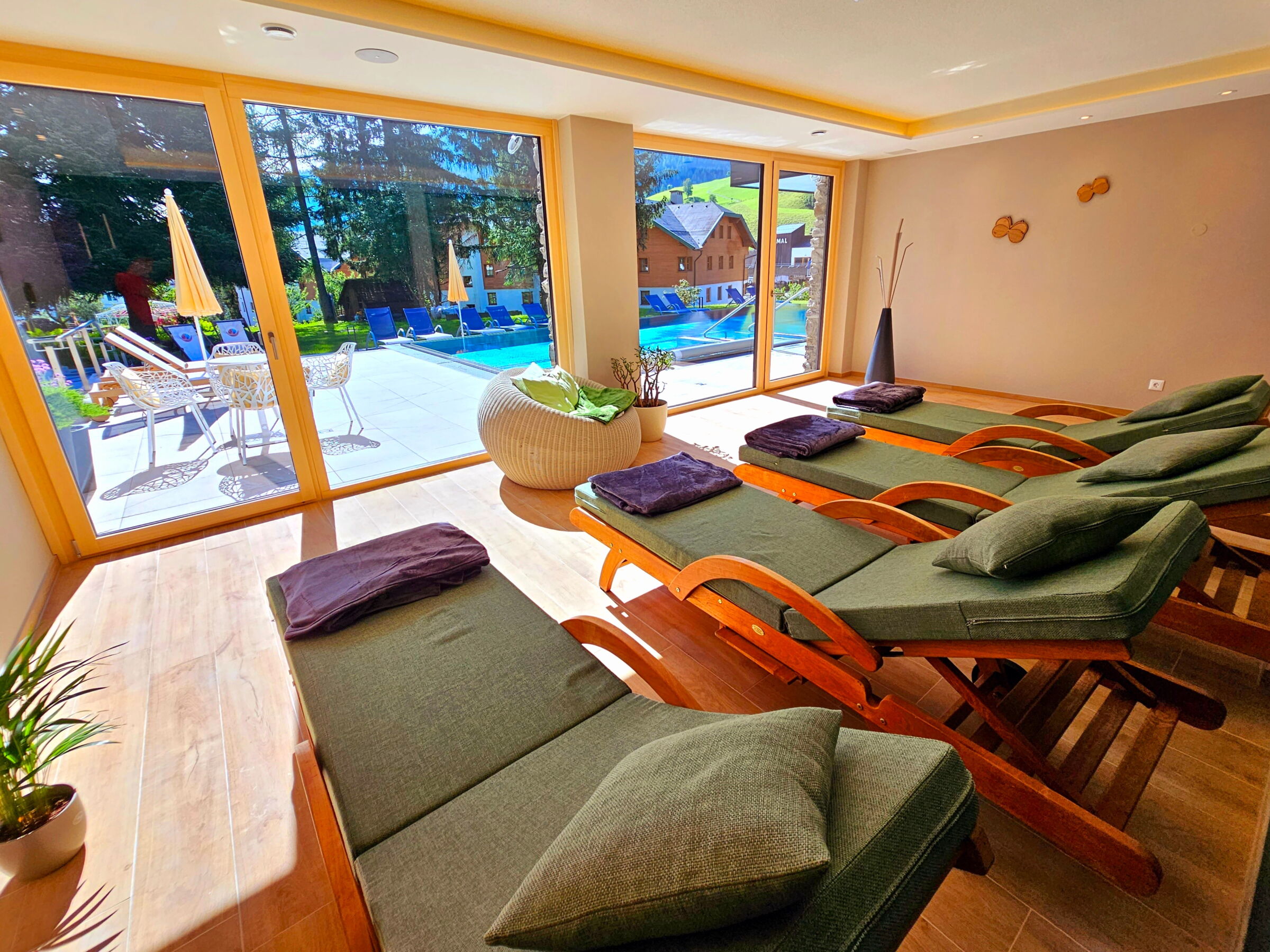 Ruhiger Lounge-Bereich mit Liegen und Blick auf den Innenpool aus großen Fenstern