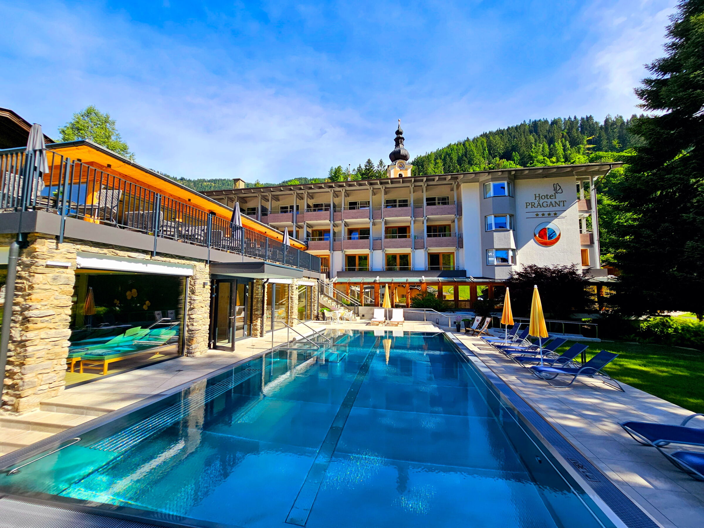 Hotel mit Swimmingpool inmitten von Bäumen und Bergen im Hintergrund zur Erholung