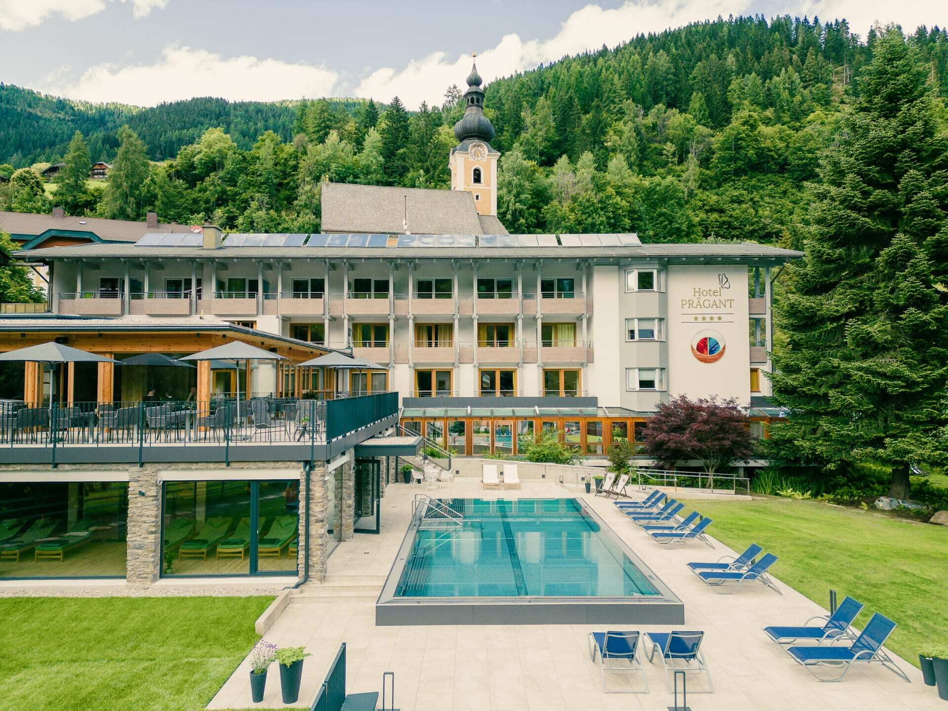 Hotel mit Schwimmbad und Liegen vor Berglandschaft und Bäumen im Freien gelegen.