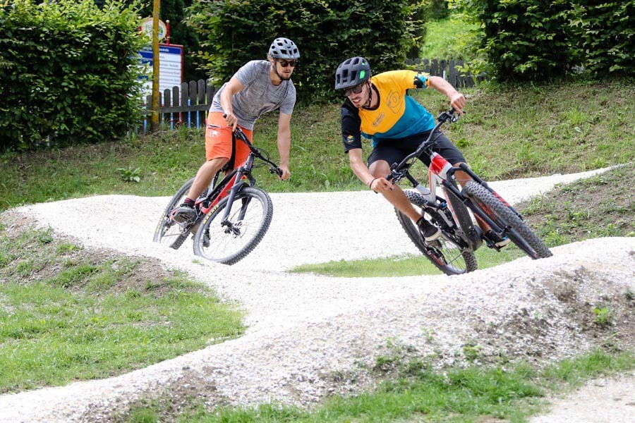 Zwei Personen fahren mit Mountainbikes auf einem Schotterweg in einer grünen Umgebung.