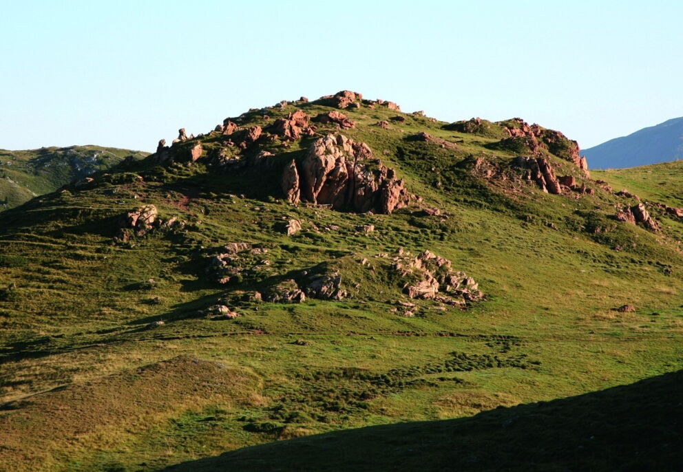 Friedliche Landschaft mit einem felsigen Hügel und grünem Gras unter klarem Himmel