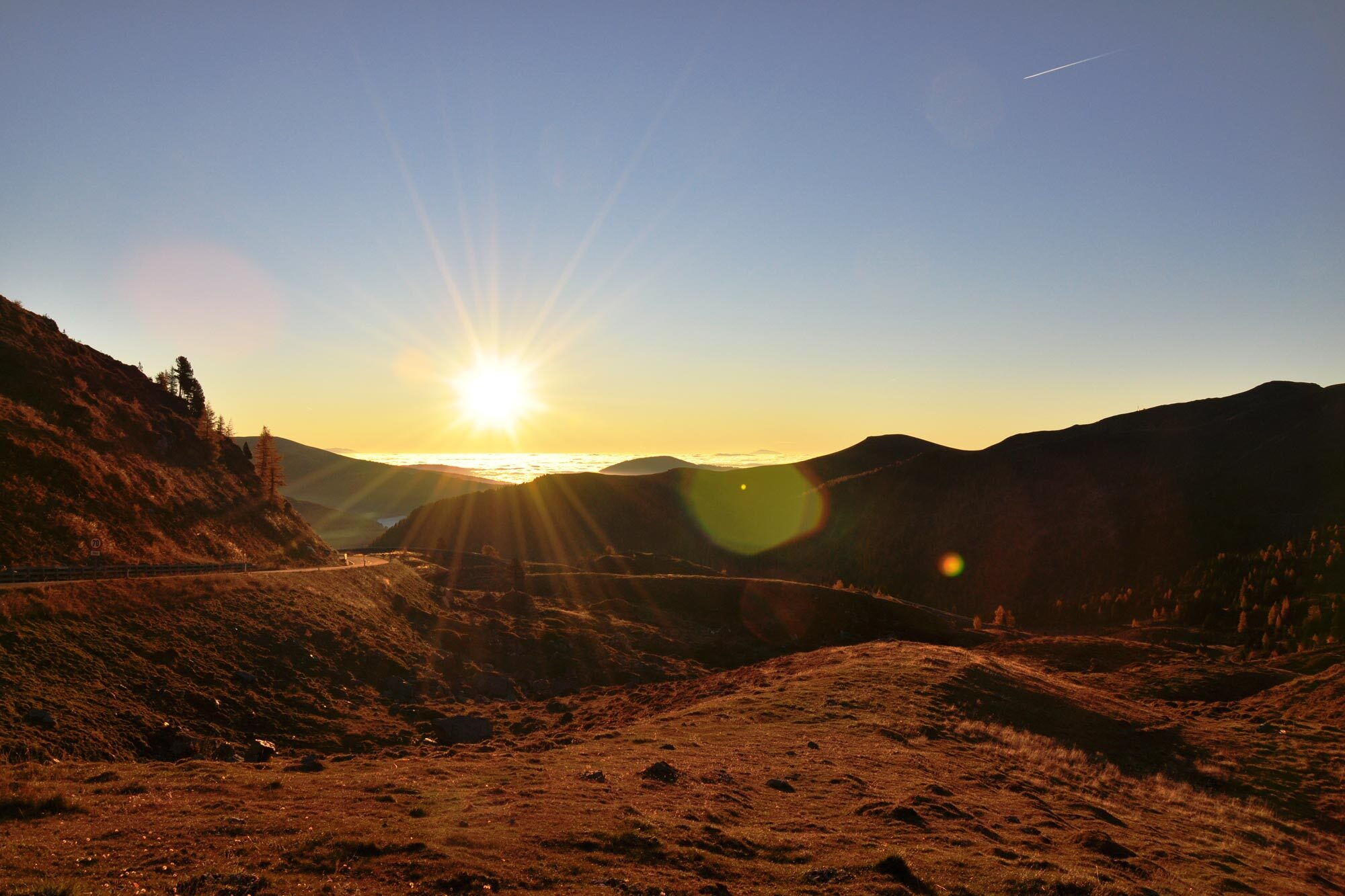 Sonnenaufgang über einer Berglandschaft in den Alpen mit klarer Sicht und warmem Licht.