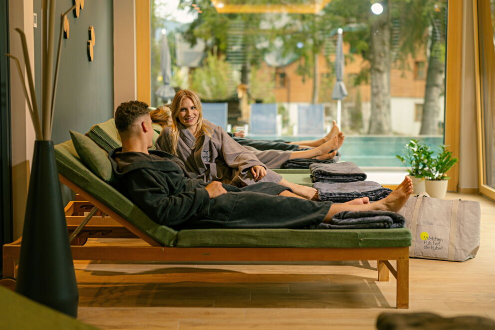 Paar in Bademänteln entspannt im Wellnessbereich mit Pool im Hintergrund und ruhiger Atmosphäre