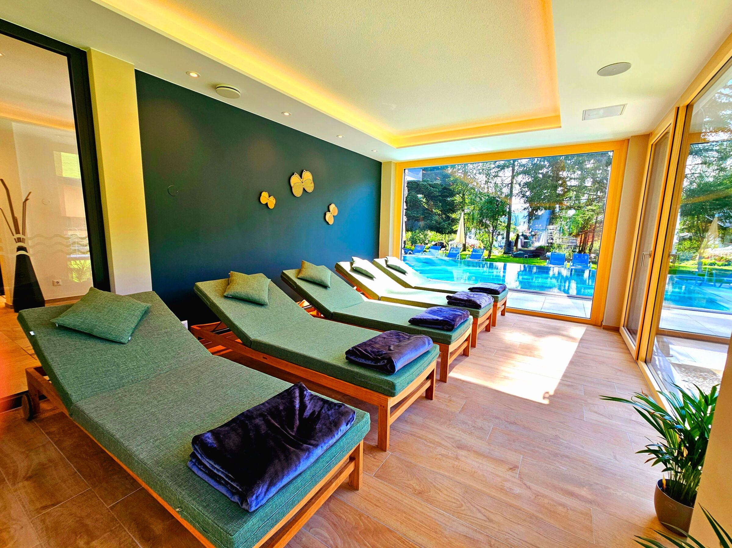 Loungebereich mit Liegen und großen Fenstern, die einen Blick auf den Pool bieten.