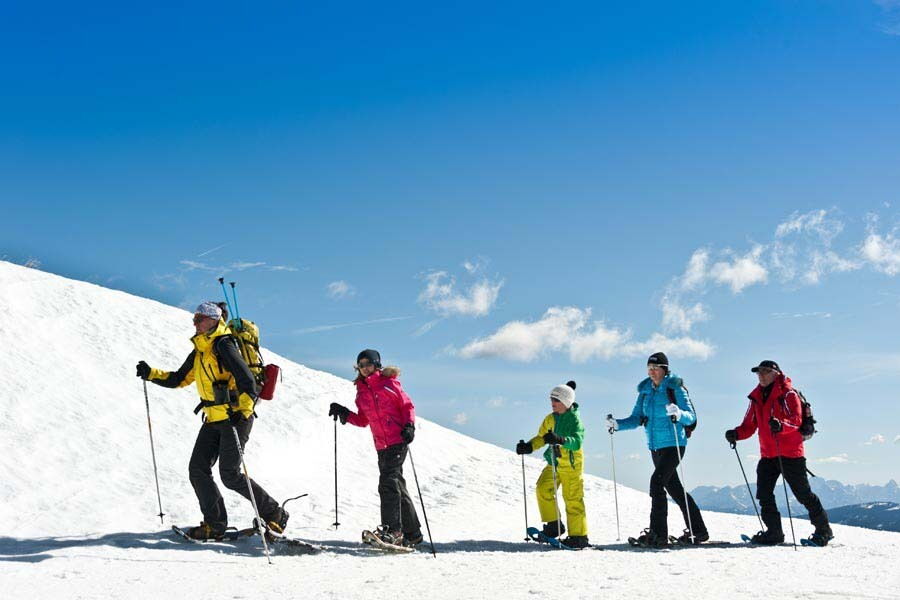 Gruppe von Personen beim Schneeschuhwandern in einer verschneiten Berglandschaft unter blauem Himmel