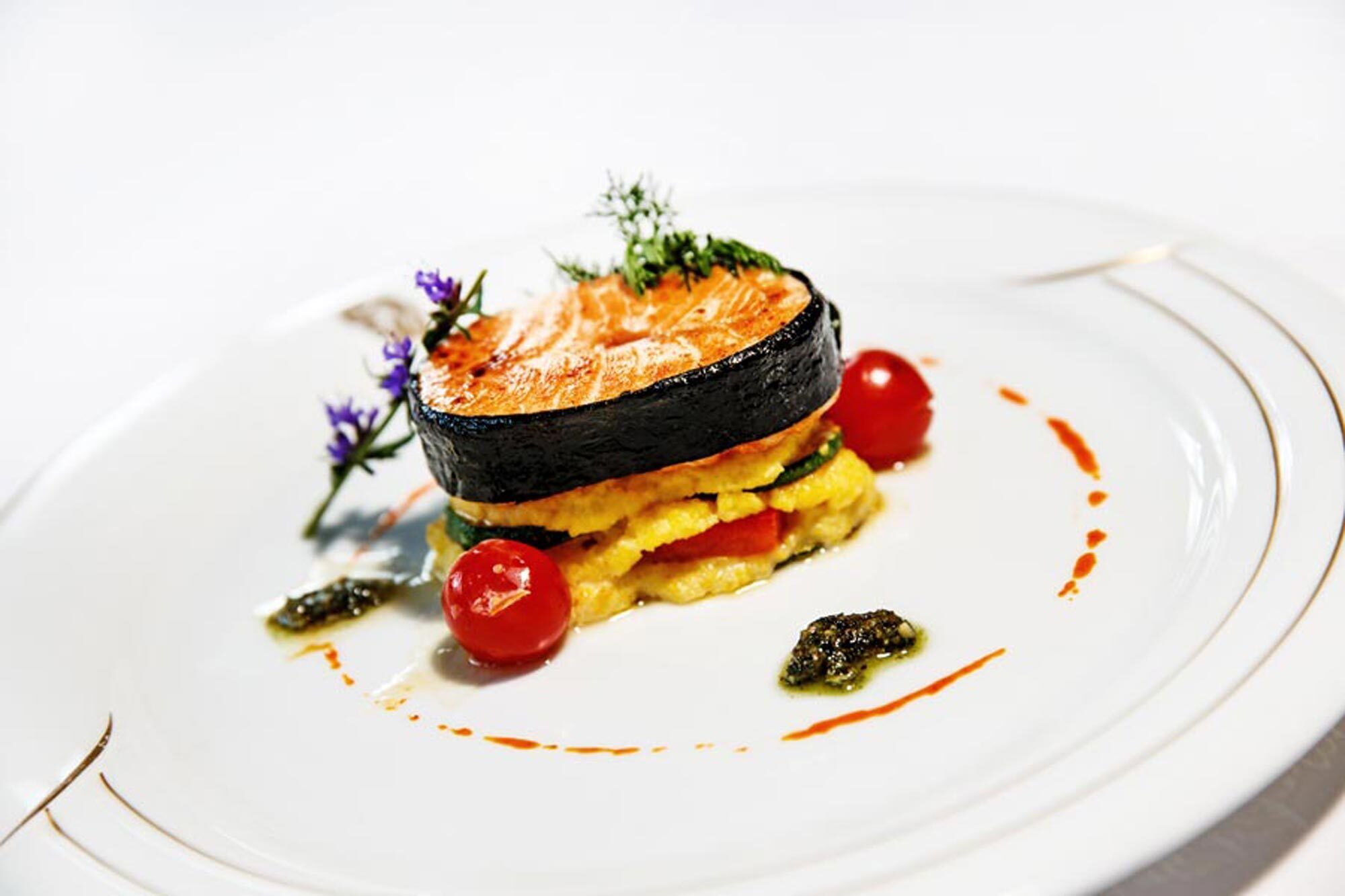 Ein fein angerichtetes Fischgericht mit Lachs und buntem Gemüse, verziert mit Kräutern und Kirschtomaten.