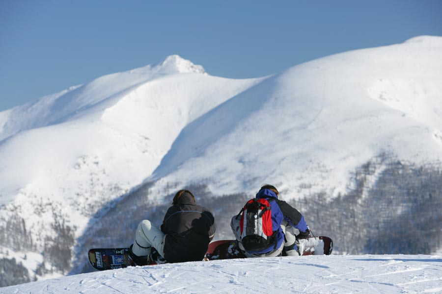 Snowboarders in the Brunnach ski area with a view of the snow-covered Alpine landscape