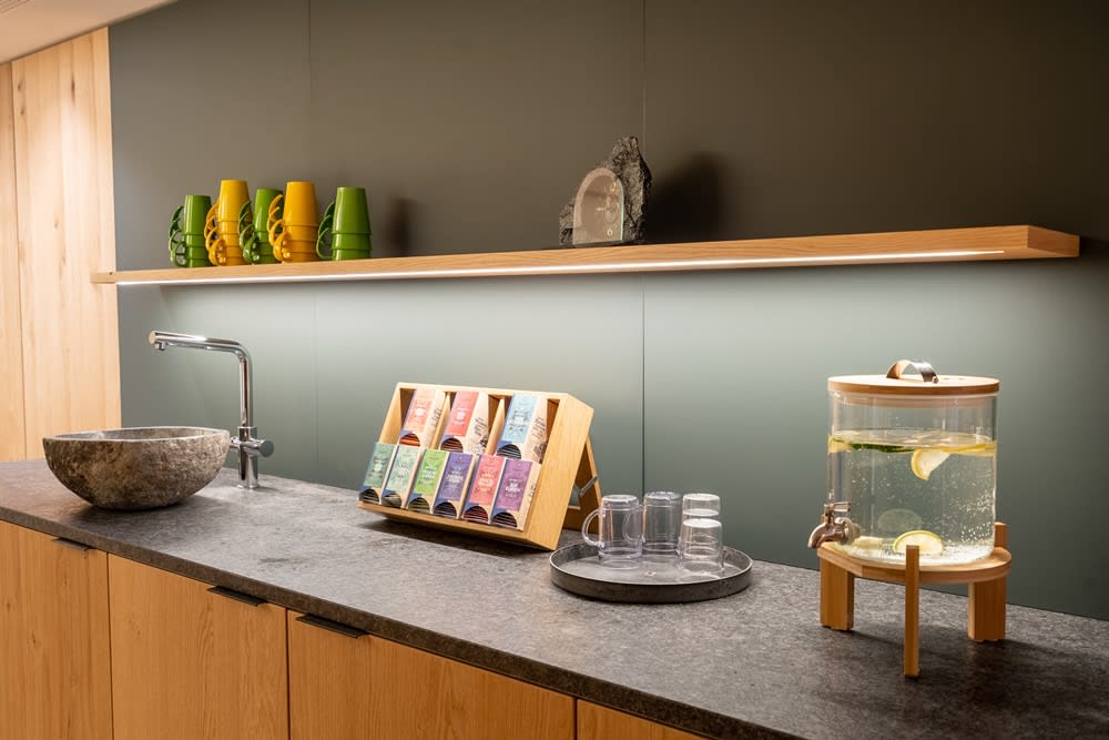 Moderne Küche mit Getränkestation, Wasserspender und Teepaketen auf einem Regal.